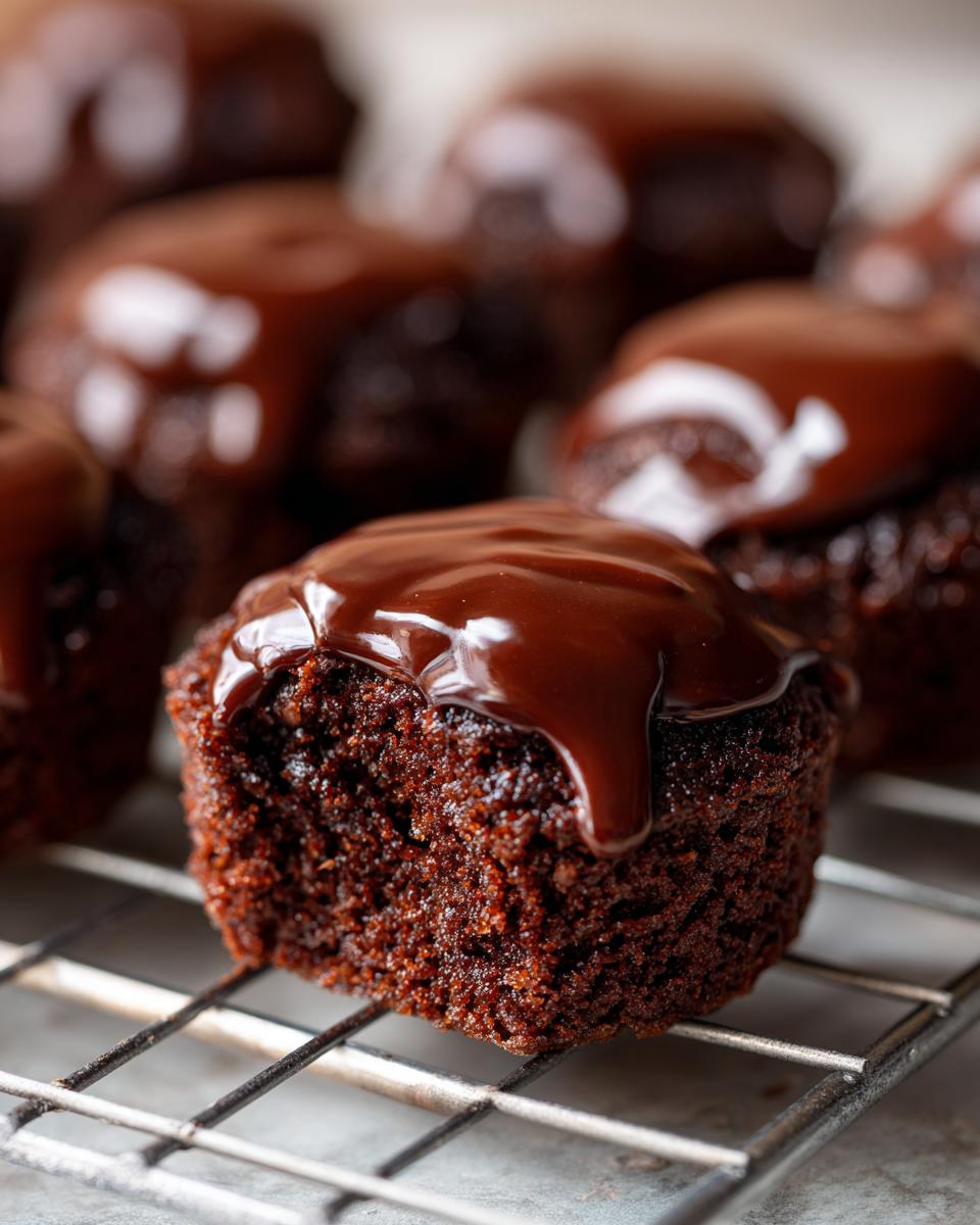 Close-up of a vegan chocolate donut hole with a bite taken out, showing its moist texture and rich chocolate glaze.