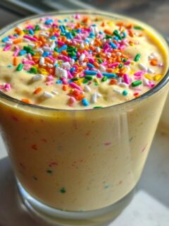 A close-up of a creamy yellow Vegan Funfetti Milkshake topped with a generous amount of colorful sprinkles.