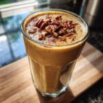 A tall glass filled with a creamy Vegan Peanut Butter Pecan Milkshake, topped with chopped pecans and a sprinkle of cinnamon.