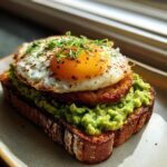 Close-up of Vegan Pesto Egg Avocado Toast featuring a fried patty, sunny-side-up egg, and chives.