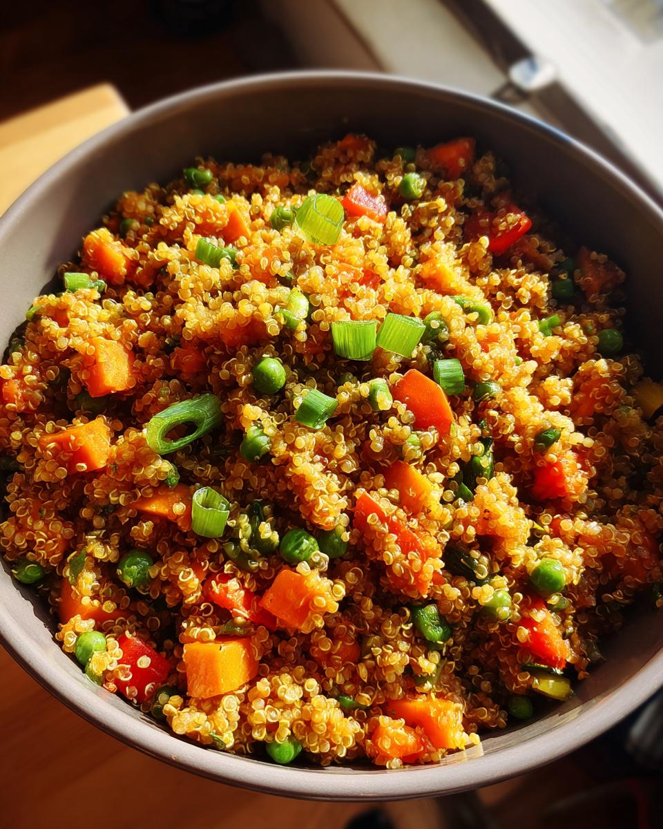 A close-up overhead view of a bowl filled with vibrant Vegan Quinoa Fried Rice, featuring colorful vegetables like peas and carrots, topped with green onions.