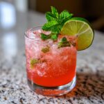 A close-up of a Watermelon Strawberry Lime Mocktail in a glass, garnished with mint and lime.
