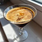 Close-up of an Apple Caramel Espresso Martini with rich foam and caramel drizzle in a martini glass.