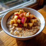 A white bowl filled with creamy Apple Cinnamon Oatmeal, topped generously with diced red apples and sprinkled cinnamon.