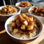 A close-up of a white bowl filled with creamy Apple Crumble Oatmeal Bowls, topped with diced spiced apples and crumble.