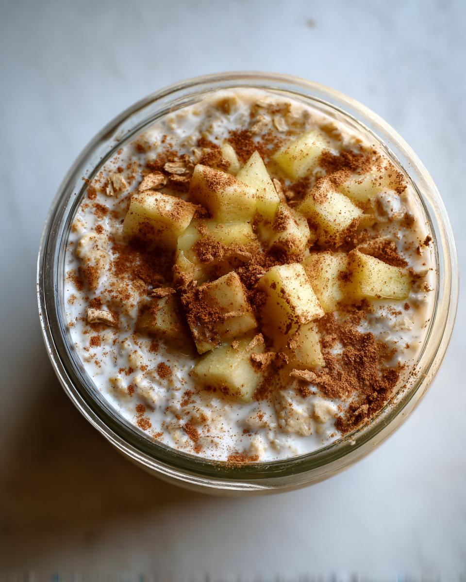 Overhead view of Apple Pie Overnight Oats topped with diced apples and cinnamon in a glass jar.