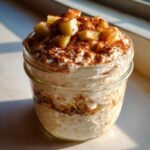 A glass jar filled with creamy Apple Pie Overnight Oats, topped with diced apples and cinnamon.