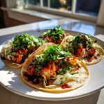 Four fully assembled BBQ Cauliflower Tacos topped with fresh cilantro and slaw on a white plate.