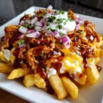 Close-up of BBQ Loaded Chicken Taco Fries topped with melted cheese, BBQ sauce, sour cream, and diced red onion.