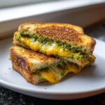 A halved Broccoli Pesto Grilled Cheese sandwich showing gooey melted cheddar cheese and vibrant green pesto filling.