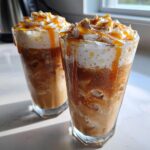 Two tall glasses filled with a layered Caramel Apple Cider Mocktail, topped with whipped cream and caramel drizzle.