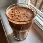 Close-up of a tall glass filled with a rich, brown Caramel Mocha Protein Smoothie topped with small, uniform foam bubbles.