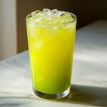 A tall glass filled with a vibrant, bright green Celery Pineapple Detox Mocktail, topped with crushed ice.