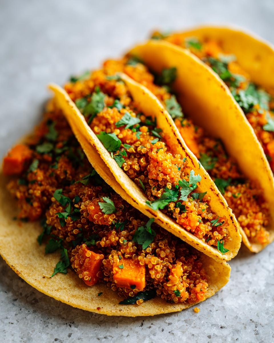 Three soft corn tortillas filled with vibrant orange Chipotle Sweet Potato Quinoa Tacos and topped with fresh cilantro.