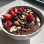 Close-up of a thick Chocolate Almond Smoothie Bowl topped with fresh raspberries, blueberries, sliced strawberries, almonds, and cacao nibs.