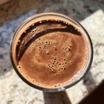 Overhead view of a rich, brown Chocolate Covered Banana Smoothie in a glass with small bubbles on top.