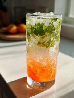 A tall glass filled with a bubbly Citrus Honey Mint Mocktail, featuring orange slices, mint leaves, and ice.