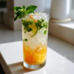 A tall glass filled with a refreshing Citrus Honey Mint Mocktail, featuring crushed ice, mint leaves, and a lime slice.