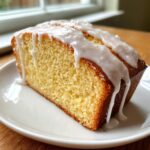 A close-up of a moist slice of Classic Lemon Pound Cake topped with thick white lemon glaze.