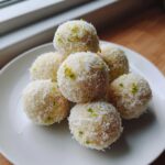 A stack of homemade Coconut Lime Energy Balls coated in shredded coconut and lime zest on a white plate.
