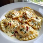 Close-up of Cozy Sun Dried Tomato Pumpkin Ravioli covered in a creamy sauce with herbs and sun-dried tomatoes.