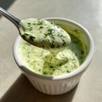 A spoonful of thick, pale green Jalapeno Ranch Sauce Dairy Free, dripping back into a white ramekin.