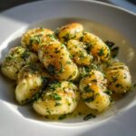 Close-up of pan-seared gnocchi coated in a rich, creamy lemon herb butter sauce with fresh parsley.