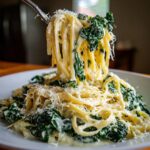 A fork lifting strands of Creamy Roasted Garlic Kale Pasta With Parmesan from a white bowl, showing rich sauce and dark green kale.