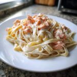 A close-up of fettuccine tossed in rich white sauce topped with flaky salmon pieces, representing Creamy Salmon Alfredo Pasta.