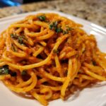A close-up shot of a serving of Creamy Tomato Basil Pasta tossed in a rich orange-red sauce and topped with chopped green basil.