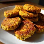 A close-up of several golden brown, baked Crispy Baked Falafel patties stacked on a white plate.