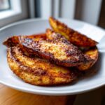 A close-up of several perfectly seasoned and Crispy Baked Jerk Potato Wedges piled on a white plate.