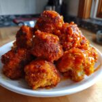 A pile of golden-brown, crispy Buffalo cauliflower bites generously coated in bright orange buffalo sauce.