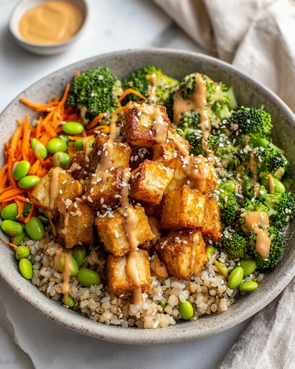 Close-up of a Crispy Tofu Buddha Bowl featuring brown rice, broccoli, edamame, and peanut sauce.