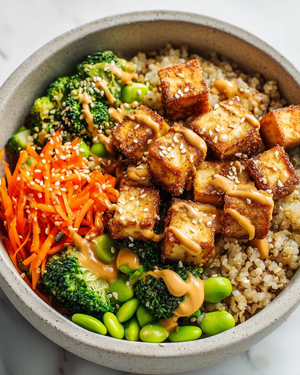 A close-up of a Crispy Tofu Buddha Bowl featuring golden tofu cubes, broccoli, shredded carrots, edamame, and peanut sauce over brown rice.