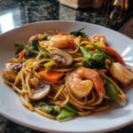 Close-up of a bowl of Date Night Healthy Shrimp Lo Mein featuring large shrimp, broccoli, mushrooms, and carrots.