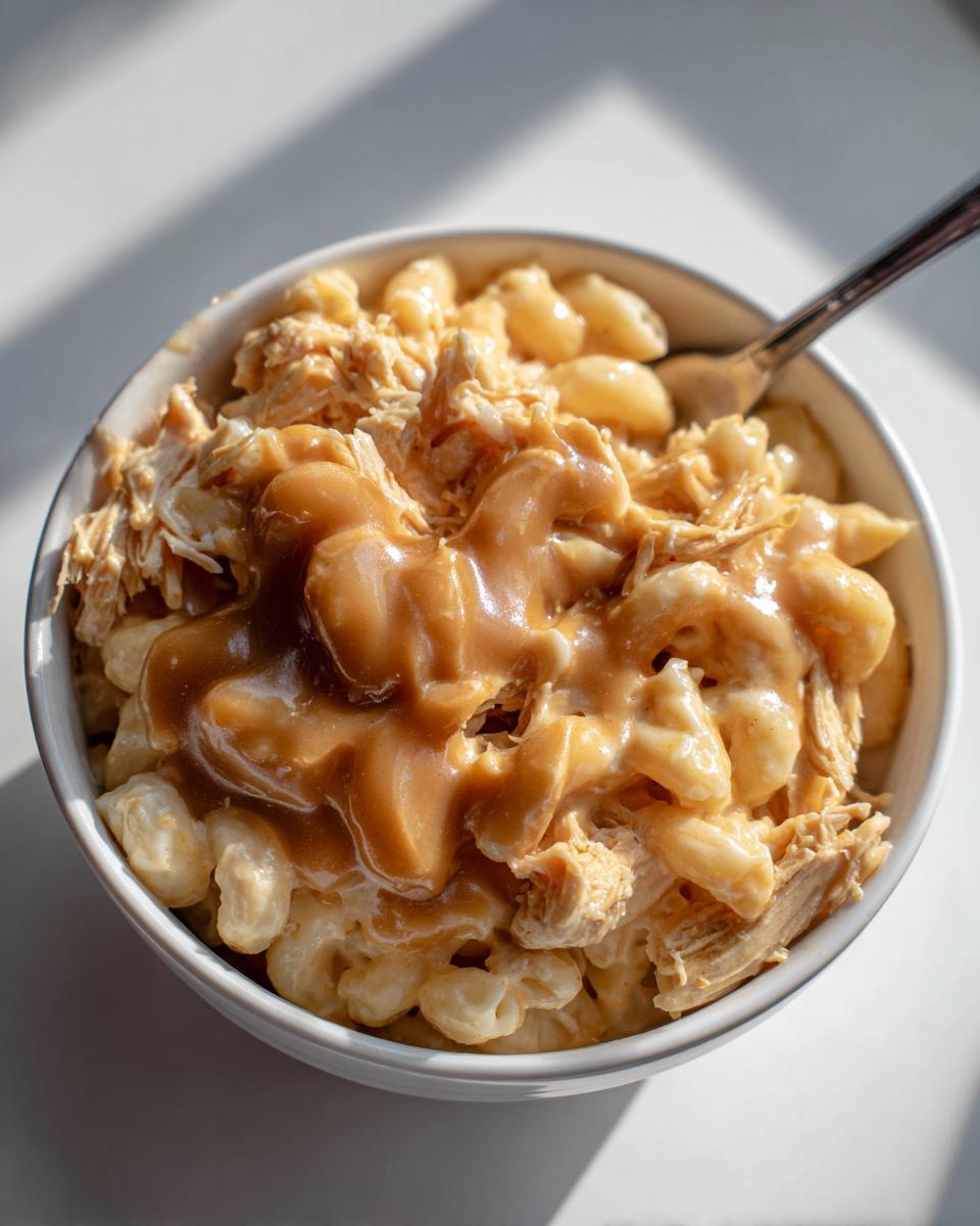 Close-up of an Easy KFC Mac Cheese Bowl Copycat featuring macaroni, shredded chicken, and brown gravy in a white bowl.