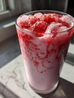 Close-up of a glass filled with Easy Quick Strawberry Milk, showing pink swirls and fresh strawberry topping.