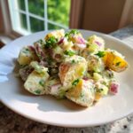 A close-up of Easy Vegan Roasted Potato Salad served on a white plate, featuring creamy dressing, red onion, and celery.