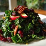 Close-up of a vibrant Fall Harvest Apple Kale Salad topped with pecans, dried cranberries, and apple slices.