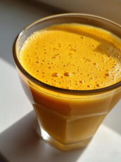 Close-up of a bright orange Healthy Pineapple Strawberry Turmeric Smoothie in a glass, catching sunlight.