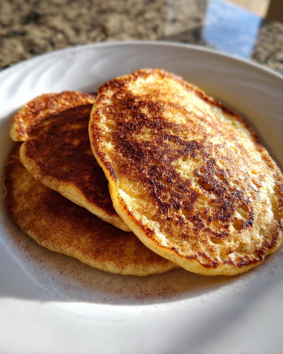 Close-up of three golden-brown Healthy Vegan Flourless Apple Pancakes dusted heavily with cinnamon.