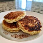 Three small, fluffy Healthy Vegan Flourless Apple Pancakes dusted heavily with cinnamon on a white plate.