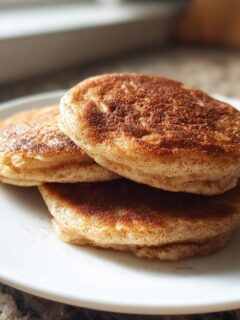A stack of three small, thick Healthy Vegan Flourless Apple Pancakes dusted heavily with cinnamon.