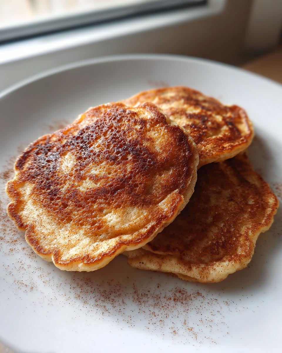 Close-up of three golden-brown Healthy Vegan Flourless Apple Pancakes dusted with cinnamon on a white plate.