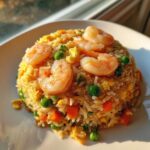 A mound of Healthy Weeknight Shrimp Fried Rice topped with plump pink shrimp, peas, and carrots.