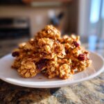 Close-up of crunchy clusters of Homemade Cinnamon Vanilla Granola mixed with dried cranberries on a white plate.