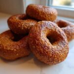 A close-up stack of five glossy, brown Homemade Pumpkin Oat Bagels sprinkled with visible oat flakes.