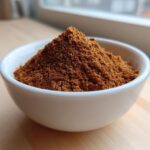 A small white bowl filled with a mound of rich brown Homemade Pumpkin Pie Spice Blend.