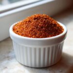 Close-up of a small white ramekin filled high with vibrant, reddish-brown homemade Taco Seasoning Recipe mix.
